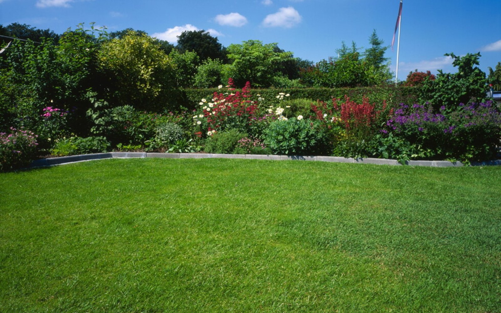 Grønn plen foran blomstrende kantbed