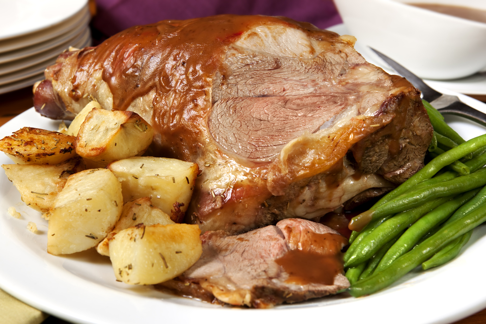 A plate of roasted meat with gravy, served alongside roasted potatoes and green beans.