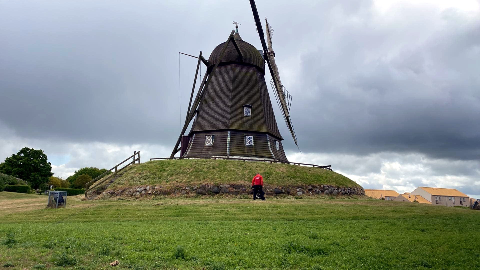 Dansk Robotklip tekniker arbejder på et stort græsareal ved en vindmølle under dansk himmel.