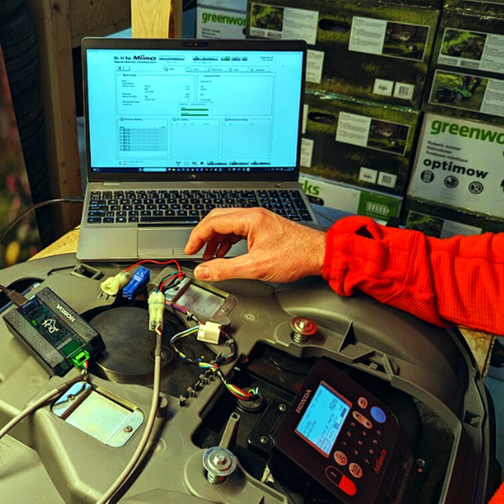 Laptop og diagnoseudstyr bruges til reparation af en robotplæneklipper.
