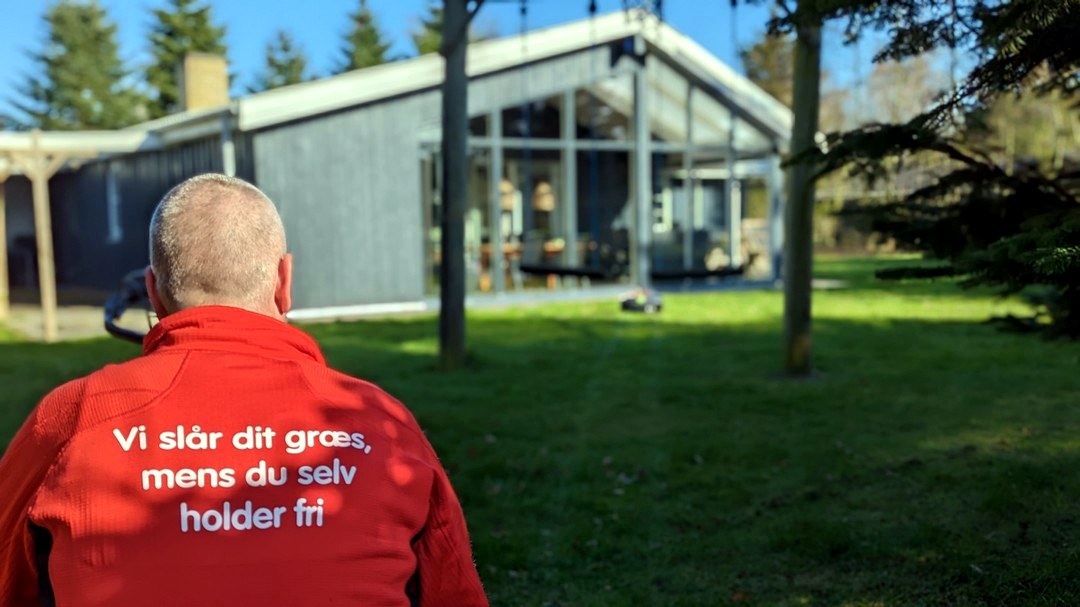 Vi slår dit græs mens du holder fri Ryggen af en Dansk Robotklip trøje med teksten om at græsset klares, mens kunden holder fri.