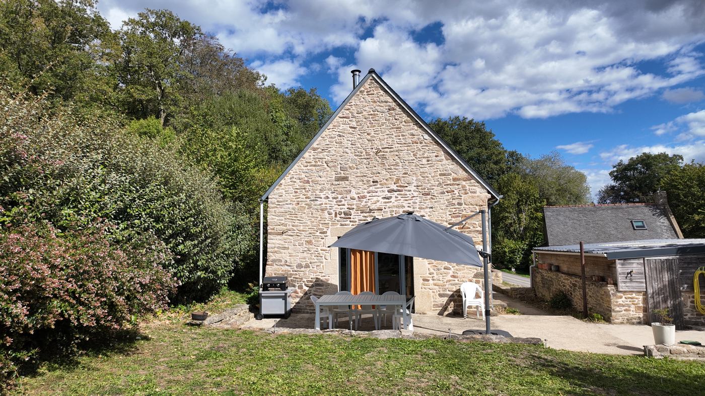 La terrasse de Kervran devant le pignon de pierre, table et parasol sous un ciel bleu