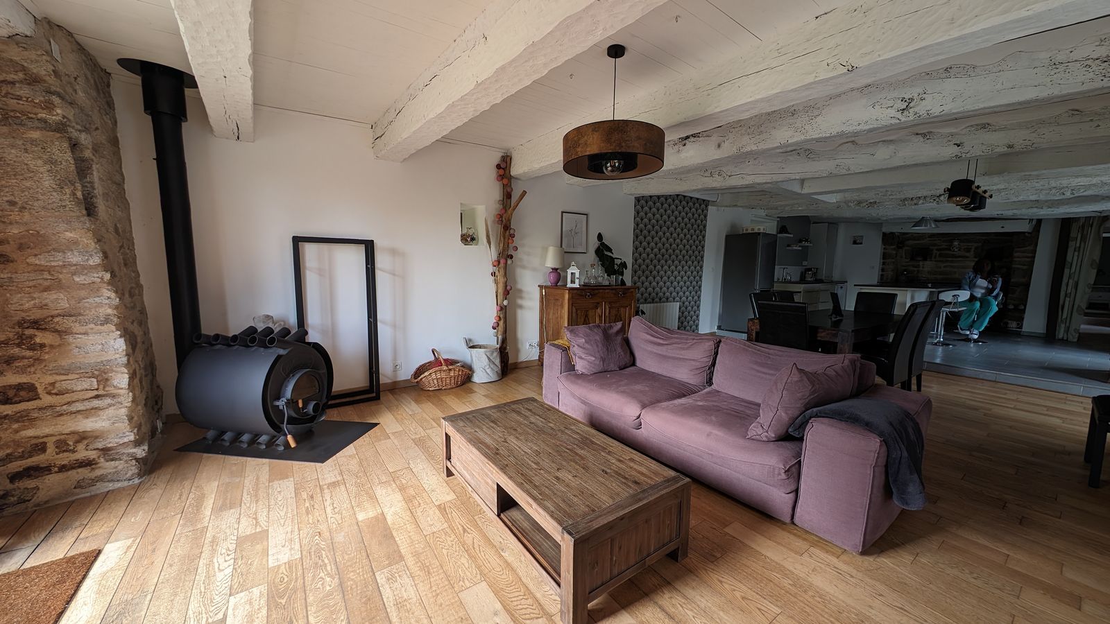 Le salon avec son poêle à bois et son canapé, devant un mur de pierre
