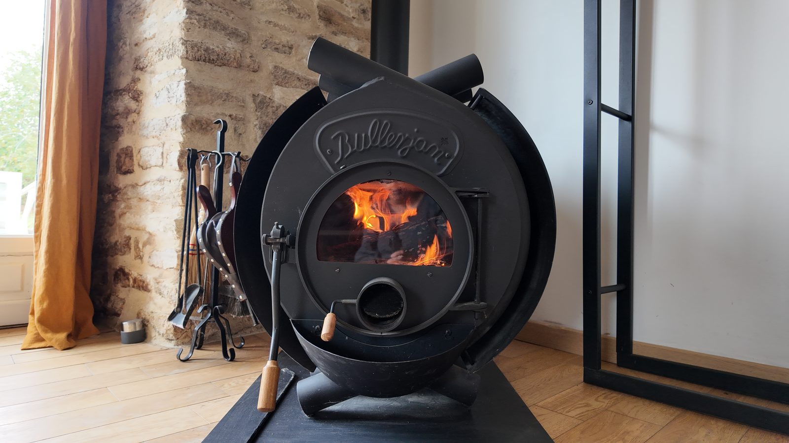 Le poêle à bois allumé, le feu visible derrière la vitre