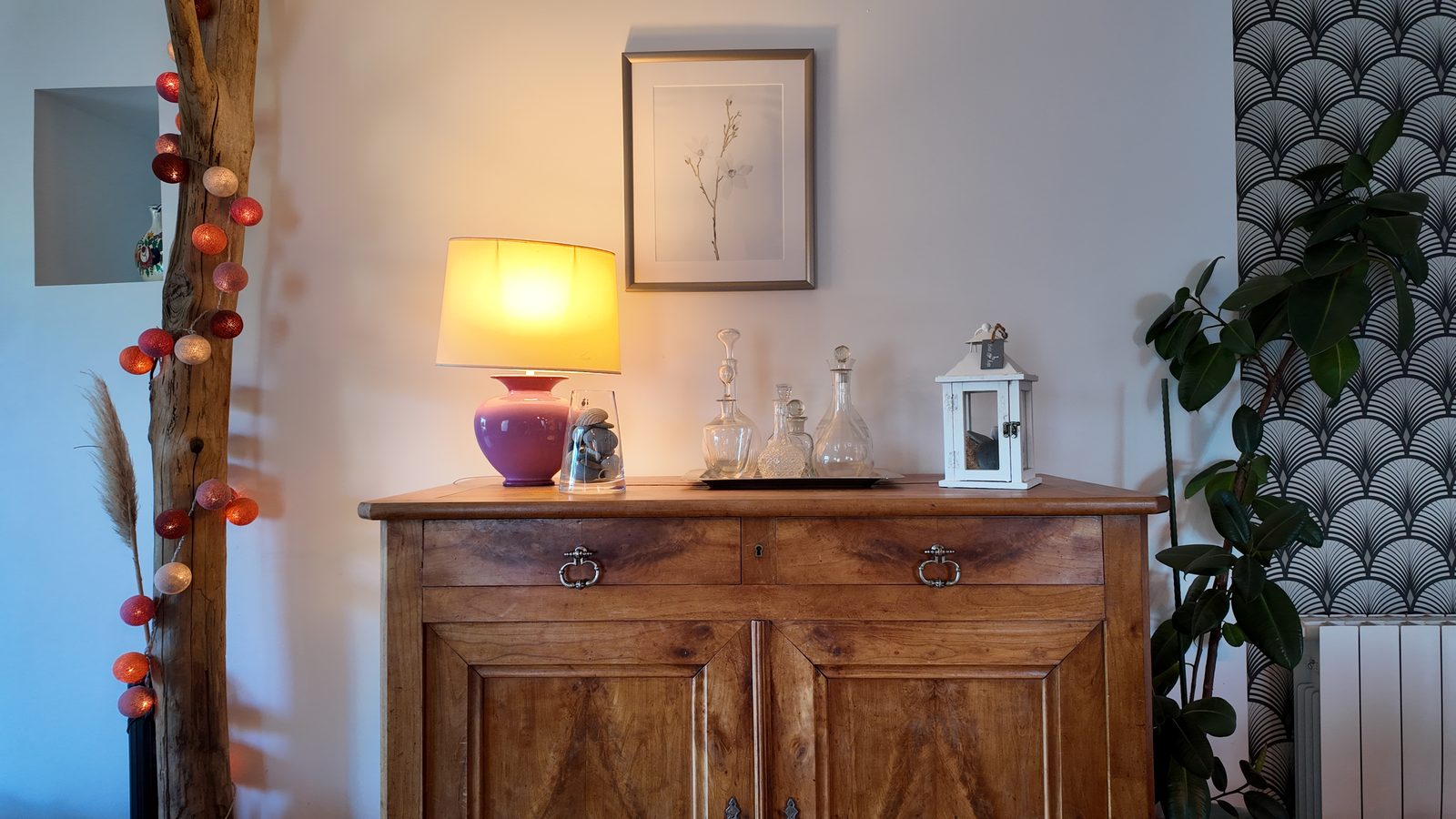 Le buffet ancien, une lampe allumée et une gravure botanique au-dessus