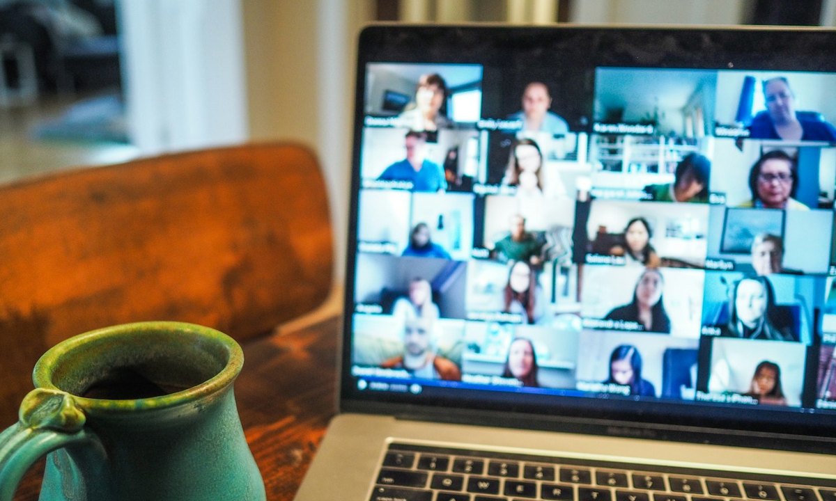 A laptop showing a video call with a full gallery of participants, next to a coffee mug