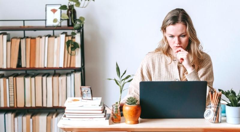 Image of a woman looking pensive while working at home on her laptop.