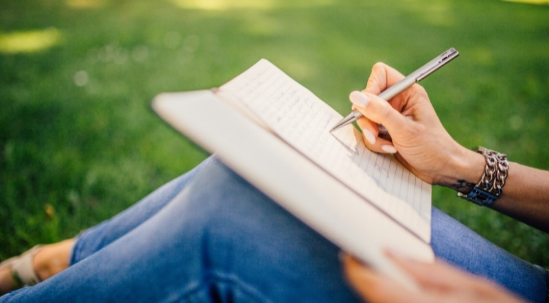 Woman sitting on grass writing in her journal.
